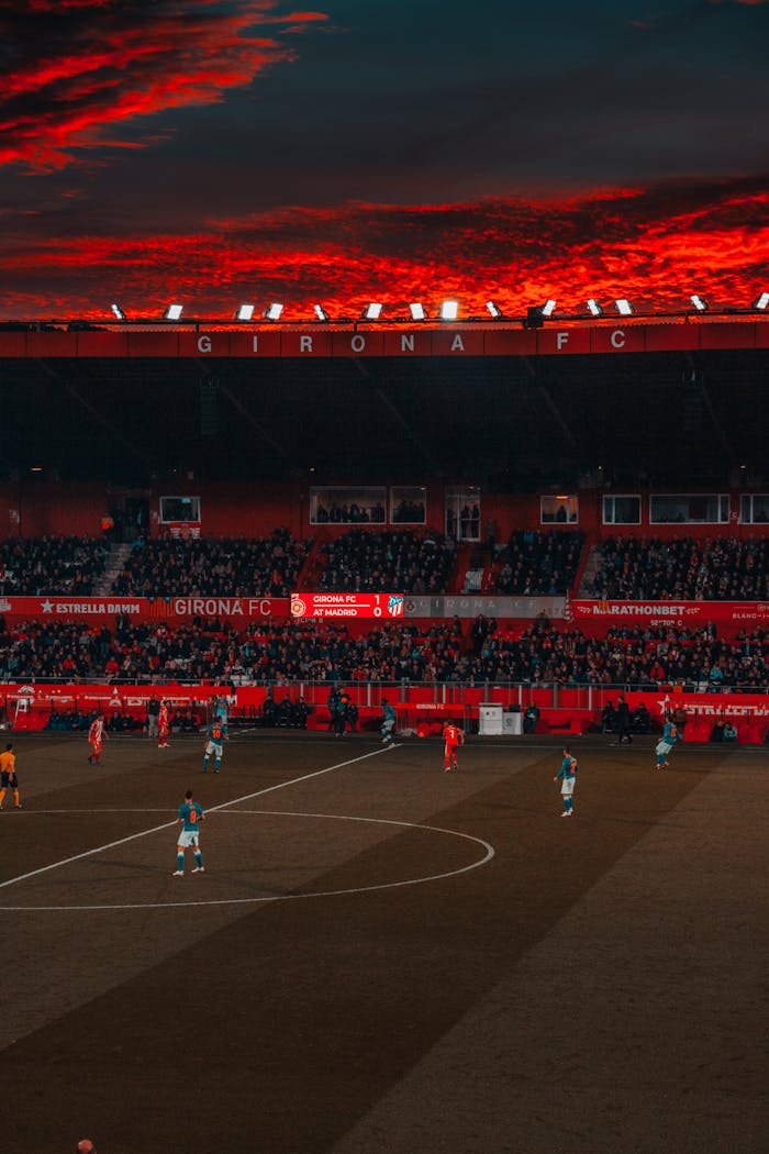 Diensten Dramatic evening soccer game at Girona FC stadium with vibrant red sky and intense play.