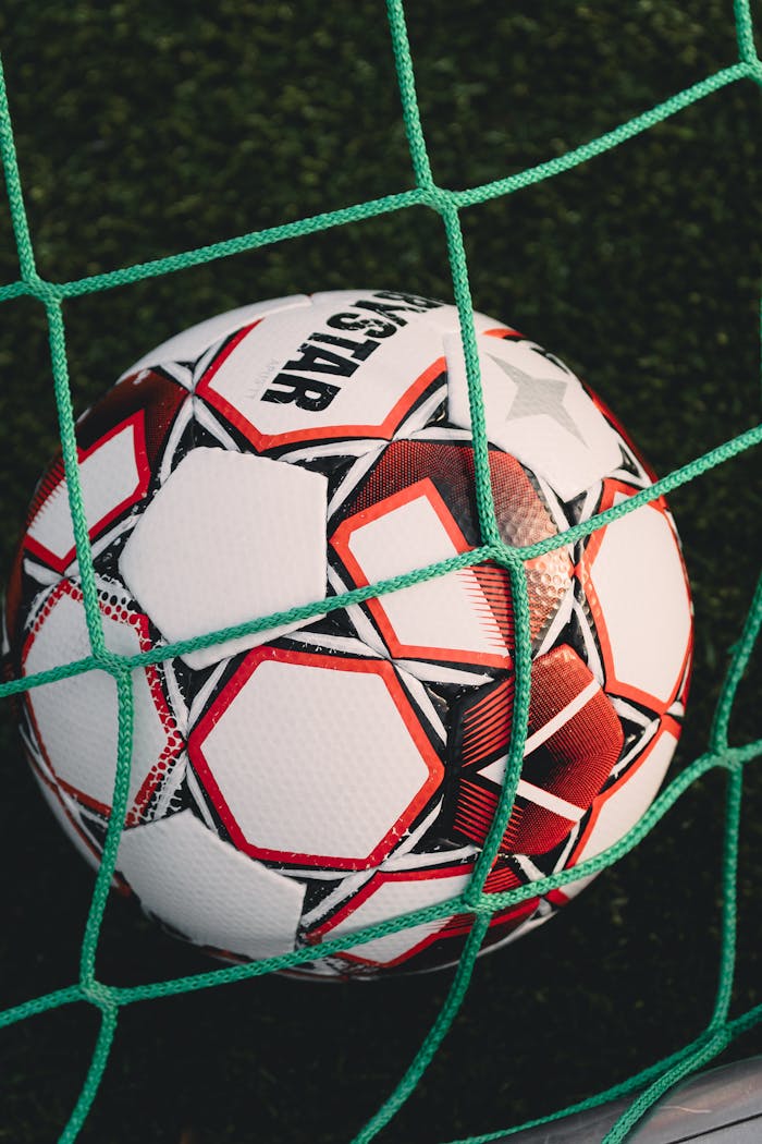 Home Close-up of a soccer ball trapped in a net on a grassy pitch, perfect for sports themes.